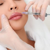 Close up of beautician hands in gloves injecting female lips with botox. Calm woman is lying with closed eyes